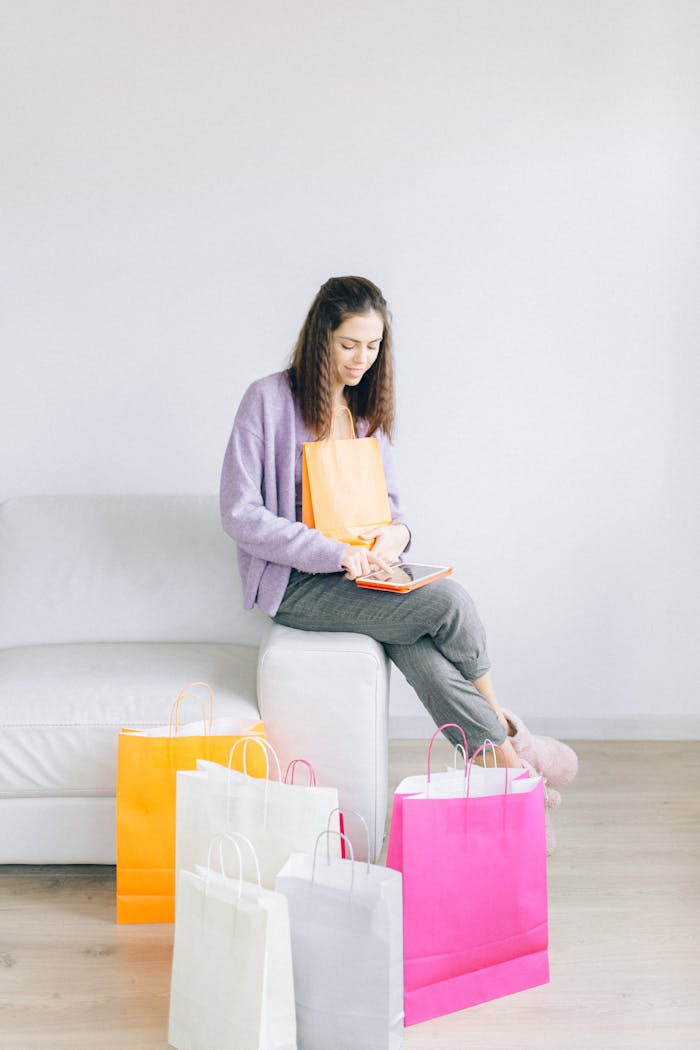Young woman sitting on a couch with tablet and shopping bags, online shopping concept.
